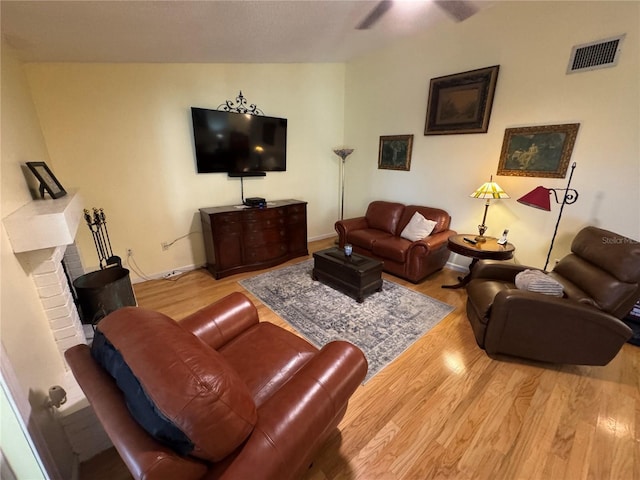 living room featuring a brick fireplace, vaulted ceiling, light hardwood / wood-style floors, and ceiling fan