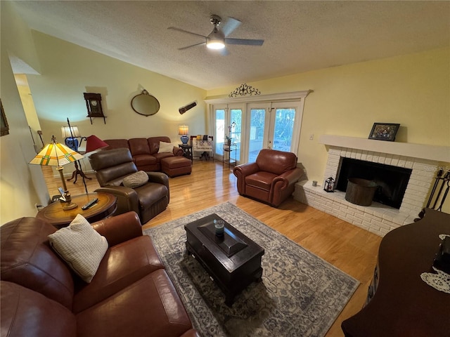 living room featuring hardwood / wood-style floors, lofted ceiling, ceiling fan, a brick fireplace, and a textured ceiling