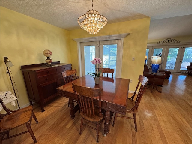 dining area featuring a chandelier, a textured ceiling, light hardwood / wood-style floors, and french doors