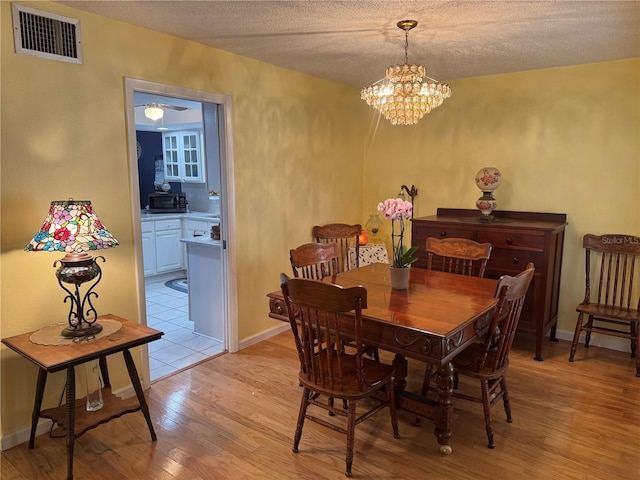 dining area featuring an inviting chandelier, a textured ceiling, and light wood-type flooring