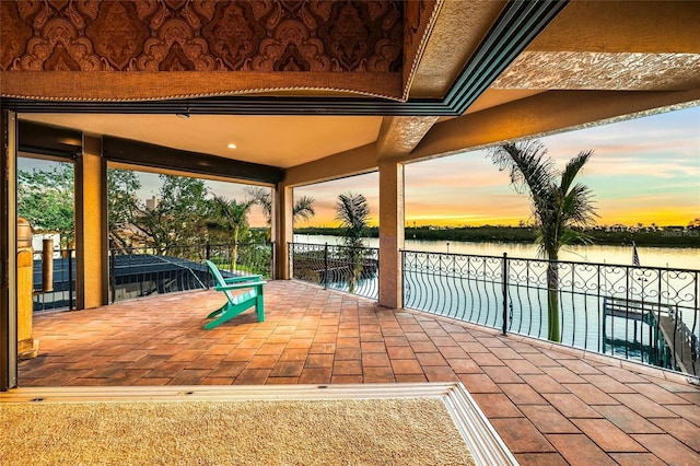 patio terrace at dusk featuring a water view and a balcony