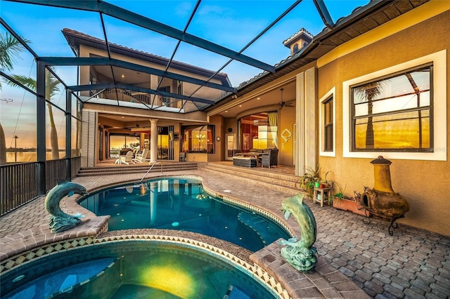 pool at dusk with an in ground hot tub, glass enclosure, ceiling fan, and a patio area