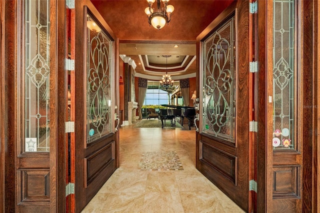 entryway with a tray ceiling, ornamental molding, and a notable chandelier