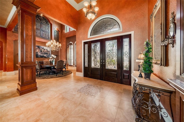 foyer with french doors, ornate columns, ornamental molding, a chandelier, and a high ceiling