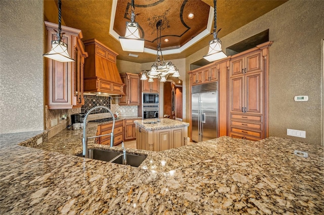 kitchen with kitchen peninsula, a raised ceiling, sink, built in appliances, and decorative light fixtures