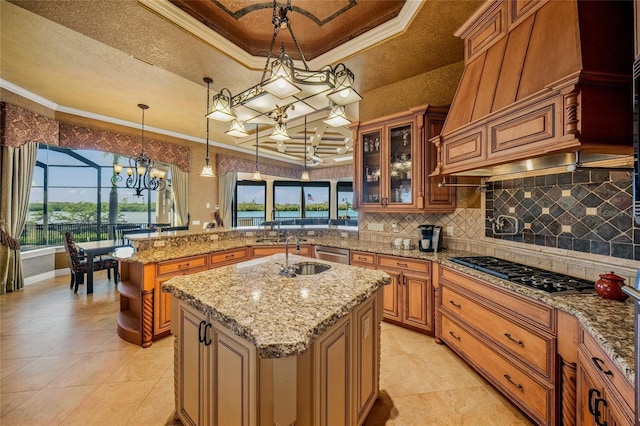 kitchen featuring stainless steel appliances, crown molding, an island with sink, decorative light fixtures, and a tray ceiling