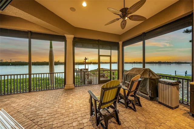 sunroom featuring decorative columns, ceiling fan, and a water view