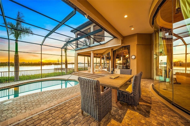 pool at dusk featuring glass enclosure, a patio area, and a water view