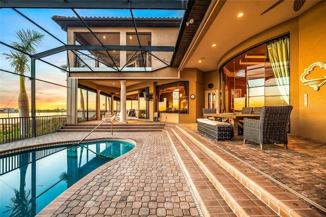 pool at dusk featuring a patio, ceiling fan, and a lanai