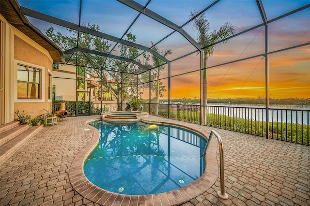 pool at dusk with a lanai, a patio area, a water view, and an in ground hot tub