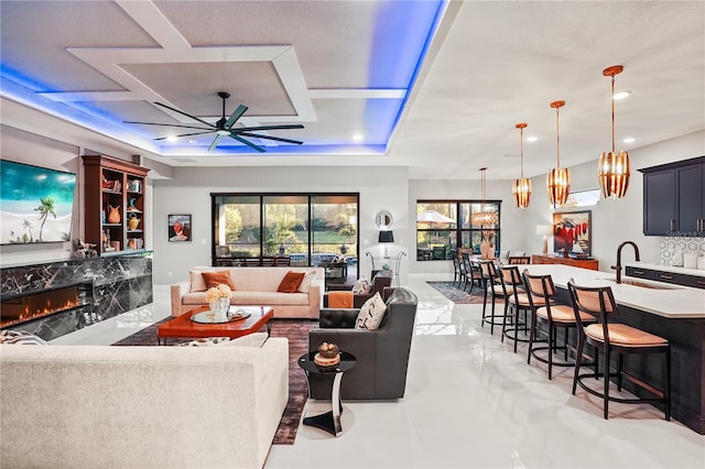 living room featuring coffered ceiling, ceiling fan, sink, and a high end fireplace