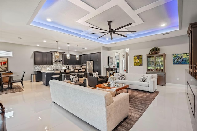 living room with a raised ceiling, coffered ceiling, and ceiling fan