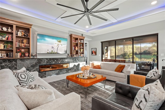 living room featuring ceiling fan, a premium fireplace, and a tray ceiling