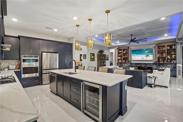 kitchen with sink, hanging light fixtures, stainless steel appliances, wine cooler, and a center island with sink