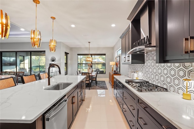 kitchen featuring pendant lighting, sink, a large island with sink, stainless steel appliances, and light stone countertops