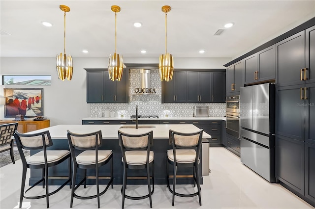 kitchen with a kitchen bar, tasteful backsplash, hanging light fixtures, stainless steel fridge, and an island with sink