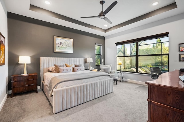 bedroom featuring multiple windows, a raised ceiling, and light carpet