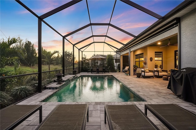 pool at dusk with area for grilling, outdoor lounge area, a lanai, ceiling fan, and a patio