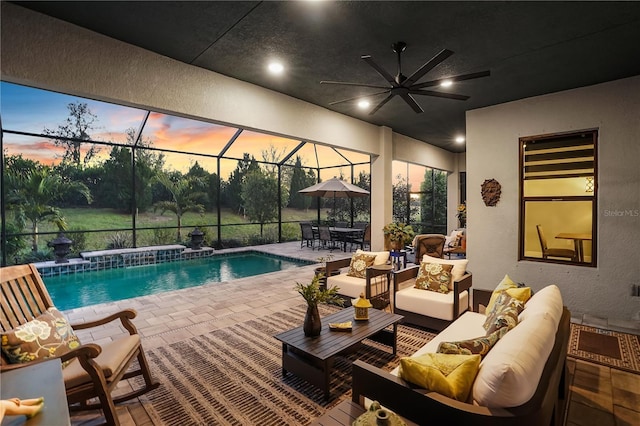 pool at dusk with ceiling fan, a patio, glass enclosure, a jacuzzi, and an outdoor hangout area