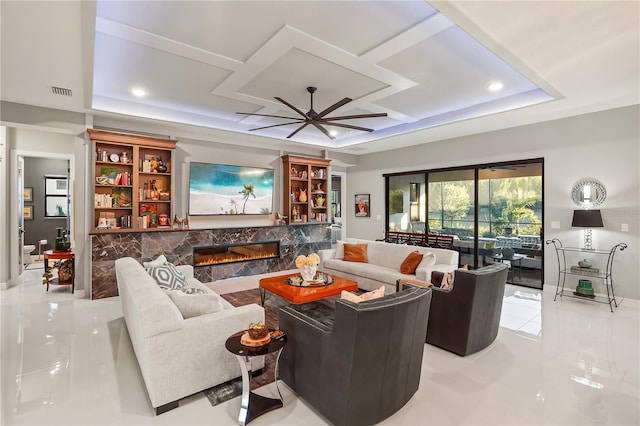 living room with coffered ceiling, a tray ceiling, a premium fireplace, and ceiling fan