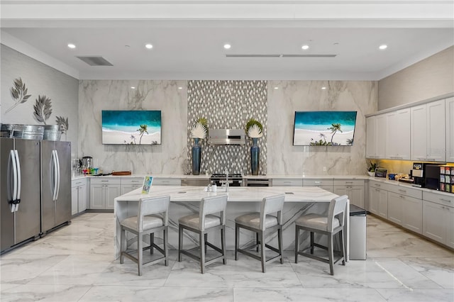 kitchen with light stone countertops, an island with sink, stainless steel refrigerator, and a breakfast bar