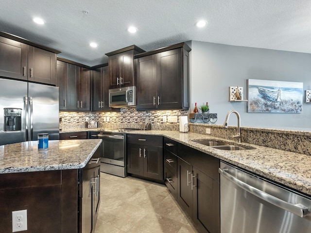 kitchen featuring light stone countertops, dark brown cabinets, a textured ceiling, stainless steel appliances, and sink