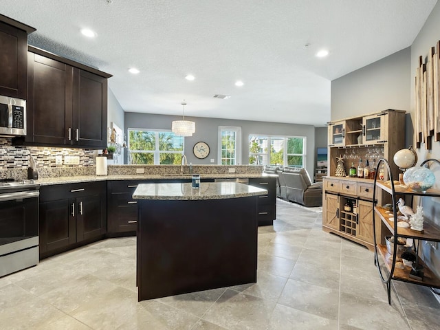 kitchen featuring a center island, backsplash, hanging light fixtures, appliances with stainless steel finishes, and light stone counters