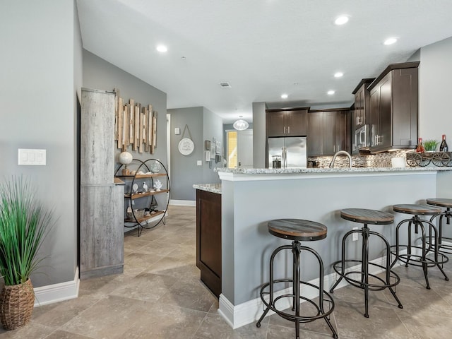 kitchen with light stone countertops, kitchen peninsula, tasteful backsplash, dark brown cabinetry, and stainless steel appliances