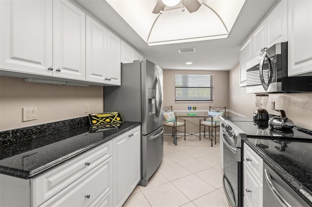 kitchen featuring white cabinets, light tile patterned floors, stainless steel appliances, and dark stone countertops