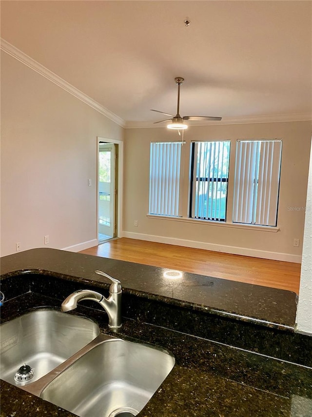 kitchen with ornamental molding, dark stone counters, ceiling fan, sink, and wood-type flooring