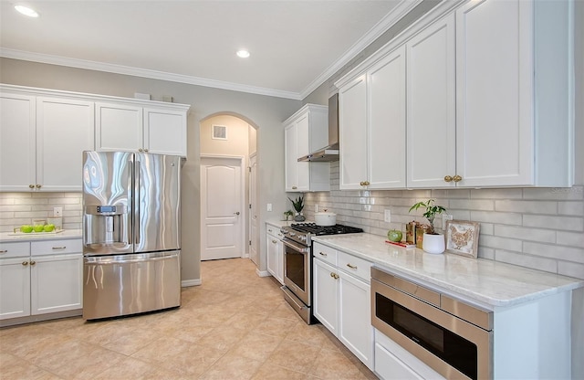 kitchen with arched walkways, light stone counters, white cabinets, appliances with stainless steel finishes, and ornamental molding