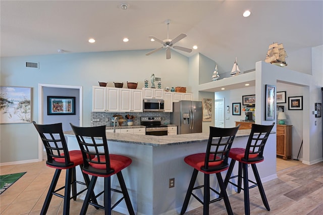 kitchen with white cabinetry, ceiling fan, stainless steel appliances, tasteful backsplash, and a breakfast bar area