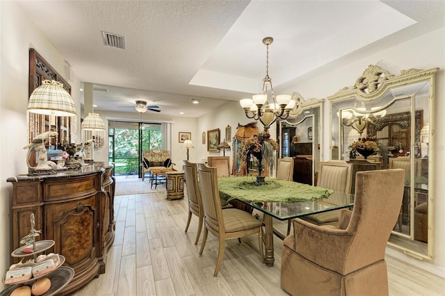 dining room featuring ceiling fan with notable chandelier, a raised ceiling, light wood-type flooring, and a textured ceiling