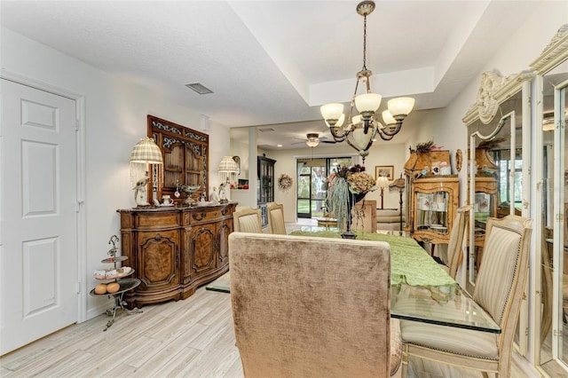 dining space with a raised ceiling, light hardwood / wood-style flooring, and ceiling fan with notable chandelier