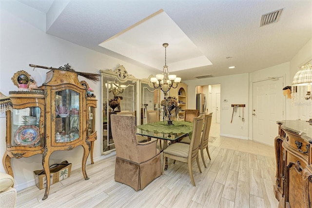 dining room with a notable chandelier, a raised ceiling, a textured ceiling, and light hardwood / wood-style flooring