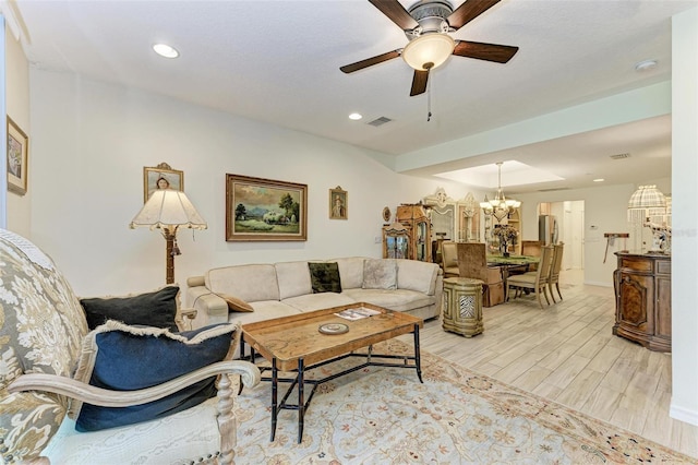 living room featuring ceiling fan with notable chandelier and light wood-type flooring