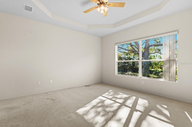 unfurnished room featuring ceiling fan, a raised ceiling, and light colored carpet