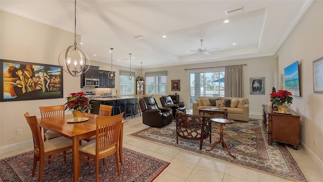 tiled dining area featuring ceiling fan with notable chandelier and a tray ceiling