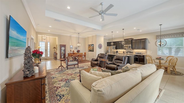 tiled living room with french doors, ceiling fan with notable chandelier, a raised ceiling, and sink