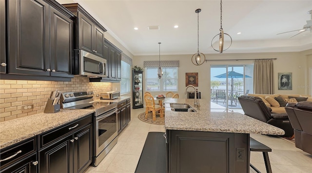 kitchen with appliances with stainless steel finishes, backsplash, a kitchen breakfast bar, sink, and an island with sink