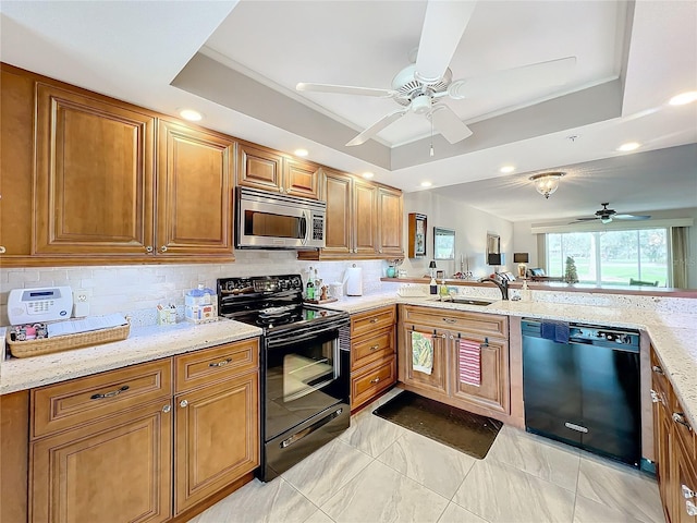 kitchen featuring backsplash, black appliances, sink, a tray ceiling, and light stone counters