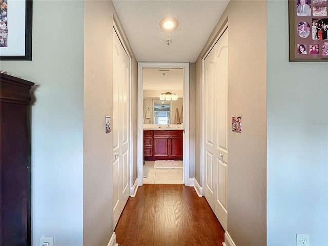 corridor with sink, wood-type flooring, and a textured ceiling