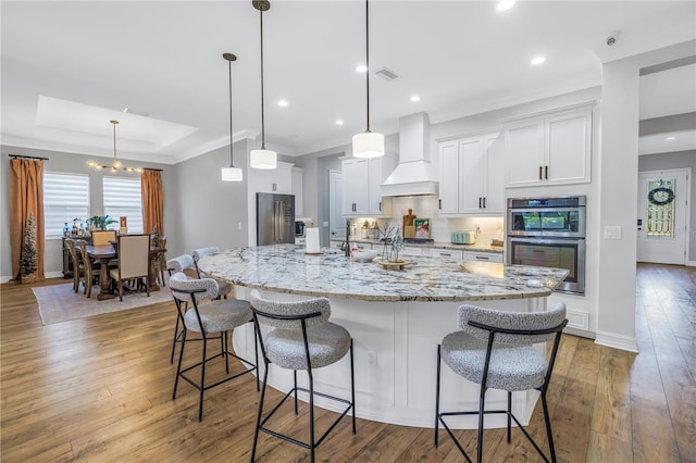 kitchen featuring white cabinets, custom exhaust hood, hanging light fixtures, and a large island with sink