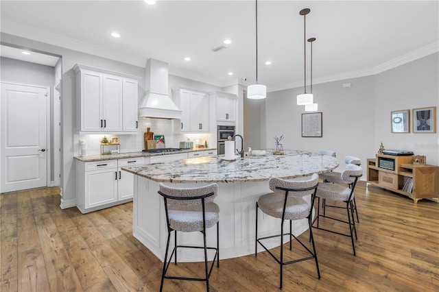 kitchen featuring premium range hood, white cabinetry, light hardwood / wood-style flooring, and a kitchen island with sink