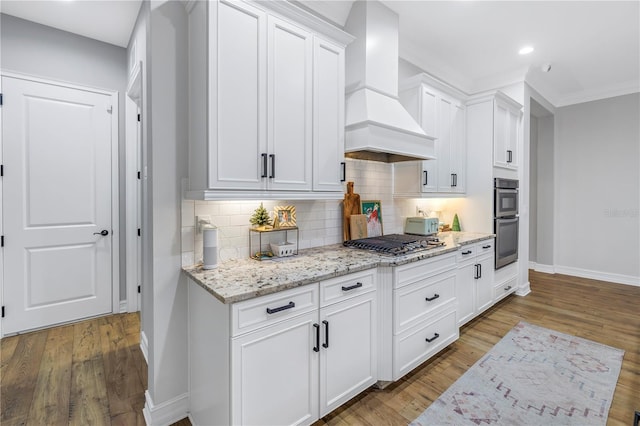 kitchen with white cabinetry, stainless steel appliances, custom range hood, and light wood-type flooring