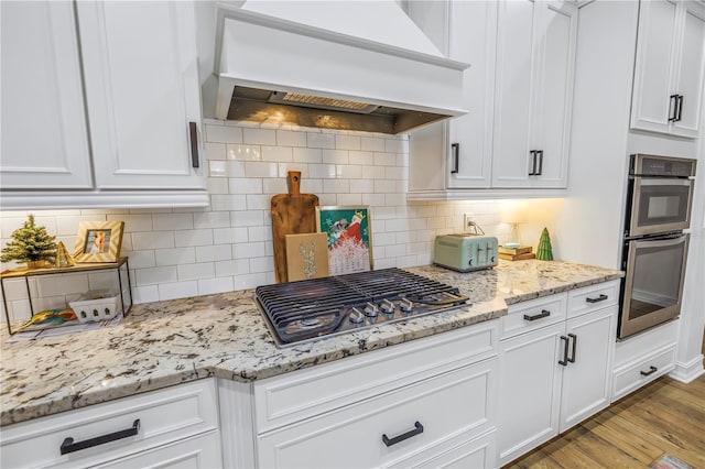 kitchen featuring premium range hood, light hardwood / wood-style flooring, white cabinets, and appliances with stainless steel finishes