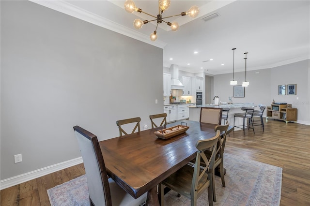 dining room featuring dark hardwood / wood-style flooring, an inviting chandelier, ornamental molding, and sink