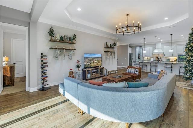 living room with hardwood / wood-style flooring, an inviting chandelier, a tray ceiling, and crown molding