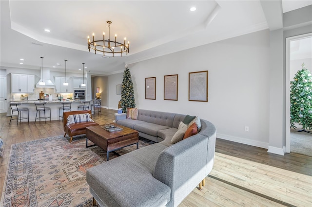 living room featuring an inviting chandelier, ornamental molding, a tray ceiling, and light hardwood / wood-style flooring