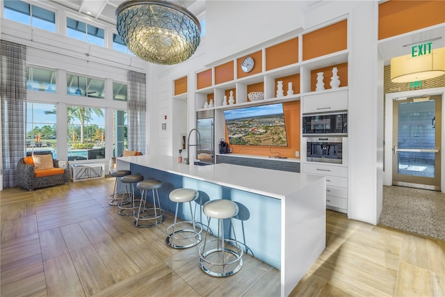 kitchen with a kitchen breakfast bar, a towering ceiling, sink, white cabinets, and an island with sink